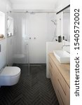 Small photo of Bathroom, with dark floor tiles designed with fish bone, wooden cabinet and elongated rectangular sink with rounded corners. Floating toilet, shower with glass doors. Hanging, long and narrow lighting