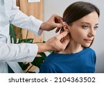 Small photo of Installation hearing aid on woman's ear at hearing clinic, close-up, side view. Deafness treatment, hearing solutions