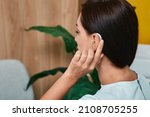Small photo of Adult woman tunes her hearing aid behind the ear by pressing her finger on setting button. Modern hearing aid, hearing solutions
