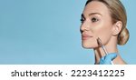 Small photo of Beautician doing beauty injection into nasolabial folds on woman face with mimic wrinkles near mouth, on blue background. Botulinum toxin injections