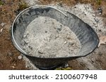 A ash bucket full of wood ashes sitting outside on the ground- Garden fertilizer- the remains of burnt firewood- A black ash bucket full of wood ash