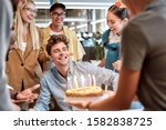 Small photo of Wish you all the best. Young cheerful man is going to blow candles on cake and make a wish while celebrating birthday with colleagues. Birthday concept. Corporate party