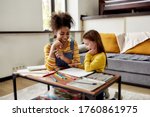 Caucasian little girl spending time with african american baby sitter. They are drawing, learning how to draw, sitting on the floor. Children education, leisure activities, babysitting concept