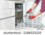 Small photo of Concept maintenance service of home appliances. Worker cleans filter in the dishwasher. Male repairman checking food residue filters.