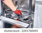 Small photo of Concept maintenance service of home appliances. Worker cleans filter in dishwasher. Male repairman checking food residue filters.