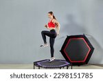 Small photo of A young athletic girl does a rebound exercise. Fitness trainer in sportswear jumps on a sports trampoline gym.