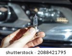 Small photo of Halogen light bulb H4 on the background of the car. A professional worker changes the new halogen lamps of the car. Car repair. The mechanic holds a halogen lamp in his hand in close-up.
