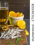 Dried salted anchovies with beer, lemon and potato chips on dark wooden board. Snack on fish with beer. Close-up.