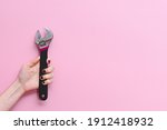 Small photo of horizontal picture of the hand of a caucasian young woman holding an adjustable monkey wrench tool on a pink background. Concept of equality at work and woman strength. Copy space on the right
