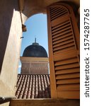 Small photo of Mariana, Minas Gerais, Brazil - September 5, 2018: View framed by the arched window with peach timber shutters over the terracotta roof to the domed bell tower Saint Peter of the Clergymen Church.