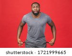 Portrait of frustrated worried african american black man with beard in casual turning out empty pockets showing I have no money gesture, bankrupt. Isolated on red background.