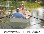 Wide shot on a happy elderly woman rowing a boat with her husband over a lake with tall grass.