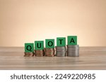 Small photo of Green wooden blocks with word QUOTA on the stacked coins