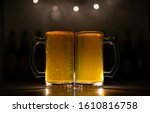 Two beer mugs filled with fresh yellow orange beer with no froth and a dark background.