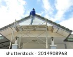back view a worker standing on a scaffolding while painting house gable background beautiful blue sky(selective focus), concept risk management, safety working at height