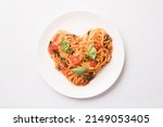 Tomato pasta with basil in a heart shape on white plate, top view, flat lay