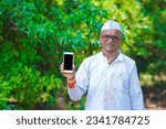 Small photo of Indian farmer shoving smartphone in farm field.
