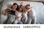 Small photo of Authentic shot of happy mother with her kids are making a selfie or video call to father or relatives in a bed. Concept of technology, new generation,family, connection, parenthood, authenticity