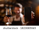 Small photo of Modern farmer or winemaker is showing in camera a smartphone with blank winery online commerce applications for checking customer service and selling orders summary of wine production in a wine cellar
