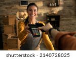 Cinematic shot of young friendly saleswoman passing pos terminal over counter to customer paying with smartphone using NFC technology in bakery shop.