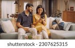 Small photo of Young Indian Couple Using Internet On Smartphone, Sitting On The Sofa at Home, they Tease and Joke around. Fun Boyfriend and Girlfriend Choosing Products, Doing Online Shopping.