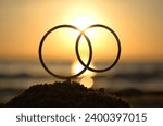 Black outlines of wedding rings at dawn and sunset on seashore. Stick contours in shape of wedding rings in sand on backdrop of setting and rising sun. Concept wedding love infatuation Valentine's Day