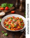 Small photo of Spicy sausages marinara pasta with parmesan cheese and fresh basil in white bowl, wooden background, selective focus