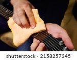 Maintenance of musical instruments. Cleaning the fretboard and guitar strings. Hands of a man wiping the fretboard of an electric guitar with a special cloth