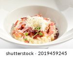 Risotto alla carbonara on white restaurant plate. Risotto with bacon and egg, garnished with micro greens. Risotto topped with parmesan cheese