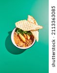 Small photo of Sausage chili with potatoes and crispy bread in minimalistic style. Mexican food on colour background with hard shadow. Chili con carne with sausage in contemporary concept. Trendy food in funky style