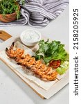 Small photo of Grilled shrimps with sauce on concrete background. Aesthetic composition with prawn skewer and fresh herbs. Shrimps on grill in summer menu. Seafood skewer in minimal style