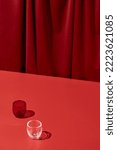 Small photo of Trendy coloured background with textile. Red background with red table and drapery textile with shadows from glass. Aesthetic red backdrop. Minimal composition with empty place on red background