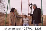 Small photo of Cheerful parents swing son into air on swing filling moment with laughter. Parents in burst of happiness propel son high into air on swing. Parents laugh and smile swinging son into air on swing