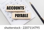 Small photo of Wooden blocks with the ACCOUNTS PAYABLE Iie on a light background on a white calculator. Nearby is a black handle. Business concept