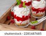 Small photo of Raspberry trifle with whipped cream, berry sauce, cookie crumbs and mint leaves in a glass on a wooden tray. Summer diet dessert