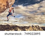 Female climber struggling up a sheer cliff.