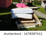 Small photo of Old furniture disjointed on a pile with a big pink teddy bear lying prone on it. The pile consists mostly of bed construction, grate and mattress covered with white sheets on a yard of a house