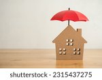 Red umbrella cover home model on office wooden table with white wall background copy space. House, real estate, property insurance business, mortgage loan insurance concept. Insurance is risk control 