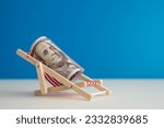 Happy US dollar bill banknote rest on wooden beach chair with blue background copy space in summer beach holiday. Financial freedom through passive income, success wealth from investment concept.