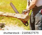 Small photo of A man saws a piece of wood with a chainsaw. Working with a gasoline chain saw, close-up. The chainsaw started moving. A young man is working with a chainsaw, sawing boards for firewood in his backyard