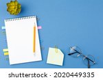 Spiral notebook with bookmarks from paper clips, note sheets, pencil, glasses and potted plant on blue isolated background. Office concept. Top view.