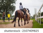 Small photo of Belarus, Vitebsk region, July 9, 2021. Children's horse riding training, on the parade ground, on the horse ranch. Horse back view. Two trainers are leading the workout.