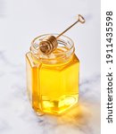 Small photo of Glass jar with floral liquid honey and metal honey spoon on light marble background. Alternative sugar substitute, cold remedy and body strengthening, superfood