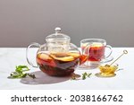 Fruit tea with apples and thyme and honey in glass teapot and cup on white background with hard shadows.