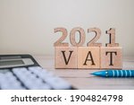 Small photo of VAT 2021 on wooden cubes, calculator and a pen on a wooden table. VAT 2021 - phrase from wooden blocks with letters, VAT 2021 concept
