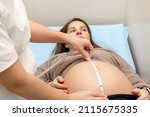 Obstetrician gynecologist measures a pregnant woman's belly with a measuring tape in medical office.Concept of pregnancy, prenatal care, medicine and healthcare.Selective focus.