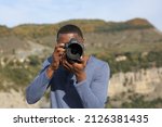 Front view portrait of a man with black skin taking photos with dslr camera in nature