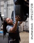 Small photo of Female car mechanic worker checking, repair and maintenance wheel at auto repair shop. African woman mechanic vehicle service maintenance examining wheel tire at garage. Auto car repair service