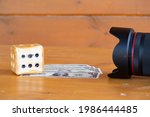 Homemade dice and dollar bills lie on a wooden table in front of a camera lens, photographers earnings
