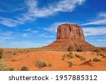 Low angle view over the red sand of the valley floor towards the Merrick Butte in Monument Valley in Utah,  United States against a white clouded blue sky